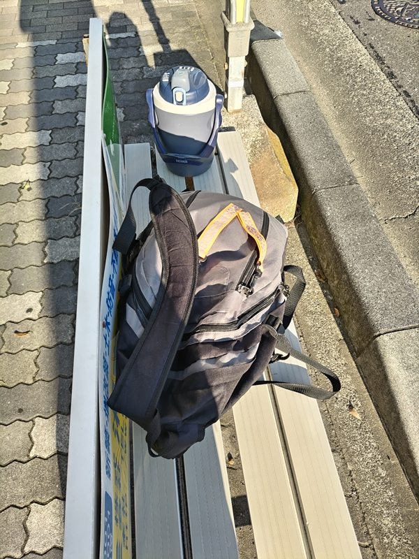 元引籠りが朝のバス停のベンチに置いた黒いリュックと水筒