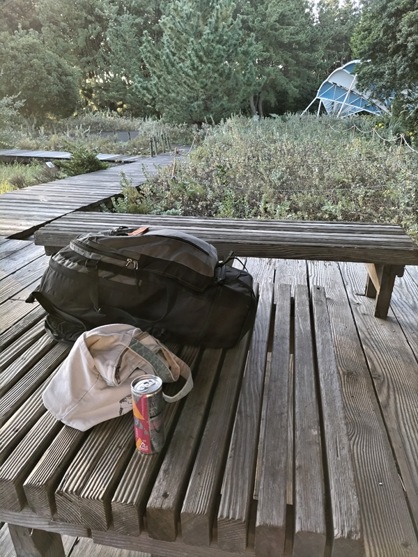 元ニートの齋藤健一が木製テーブルの上に置かれたリュックと栄養ドリンクを見ている様子