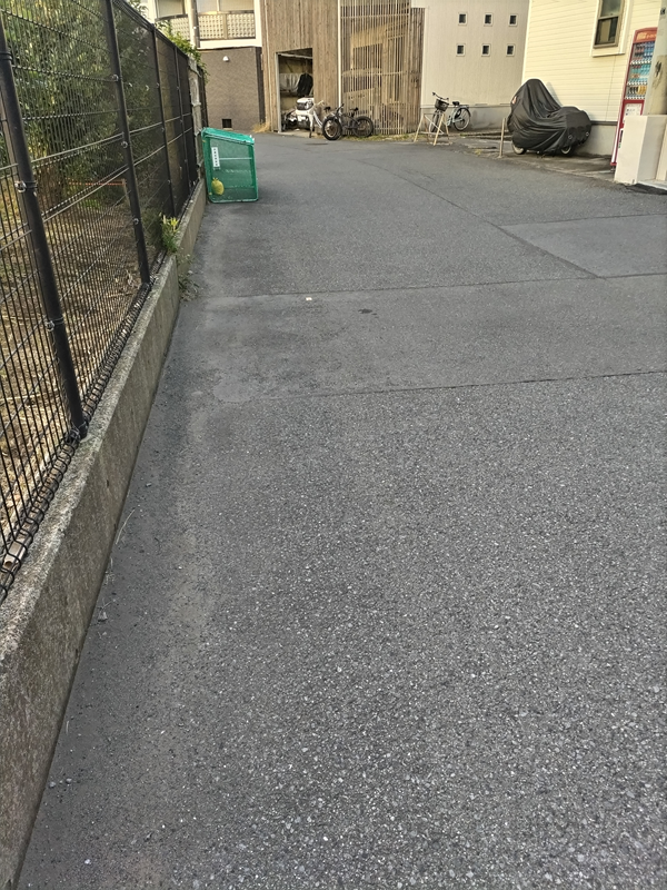 引籠りニートだった齋藤健一が朝のアスファルトの道路上にある緑色のごみ入れを見ている様子