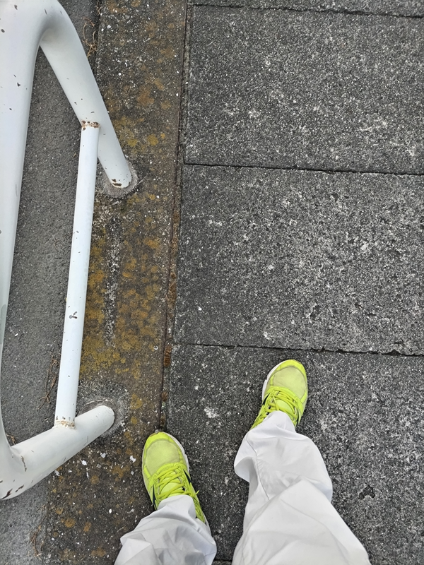 元引籠りのニートだったセル齋藤が白いズボンと黄色いスニーカーを履いてコンクリートの地面を歩いている様子