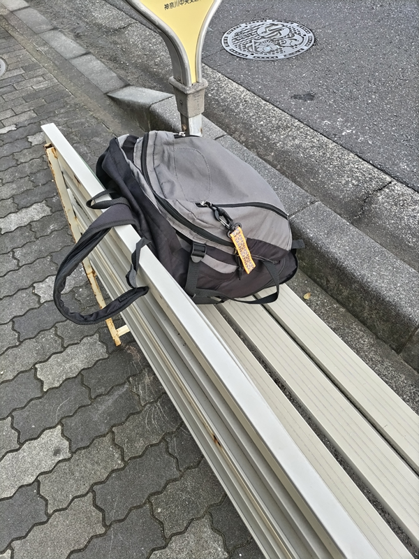 元ニート引籠りがバス停前の白いベンチに置いた灰色のリュック