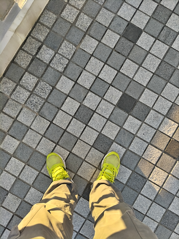 元ニートが黄色いスニーカーを履いて夕方にタイル張りの地面に立っている様子